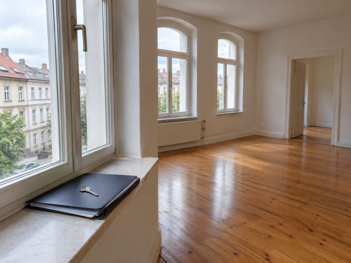 Leere Altbauwohnung mit Dielenboden, auf der Fensterbank eine Mappe mit Unterlagen und ein Schlüssel